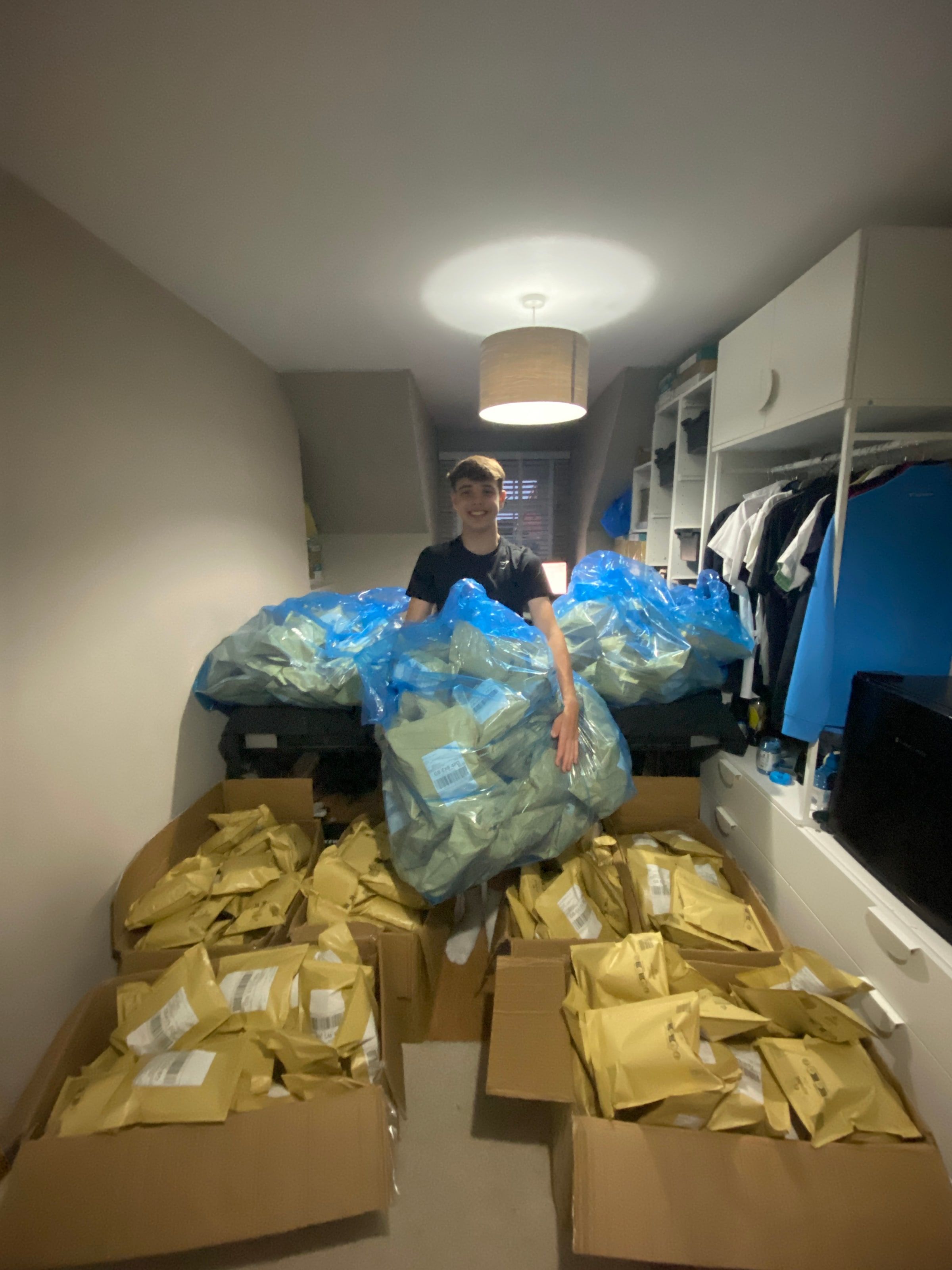 Harrison standing behind a bed covered in Royal Mail sacks, with four cartons of parcels on the bedroom floor