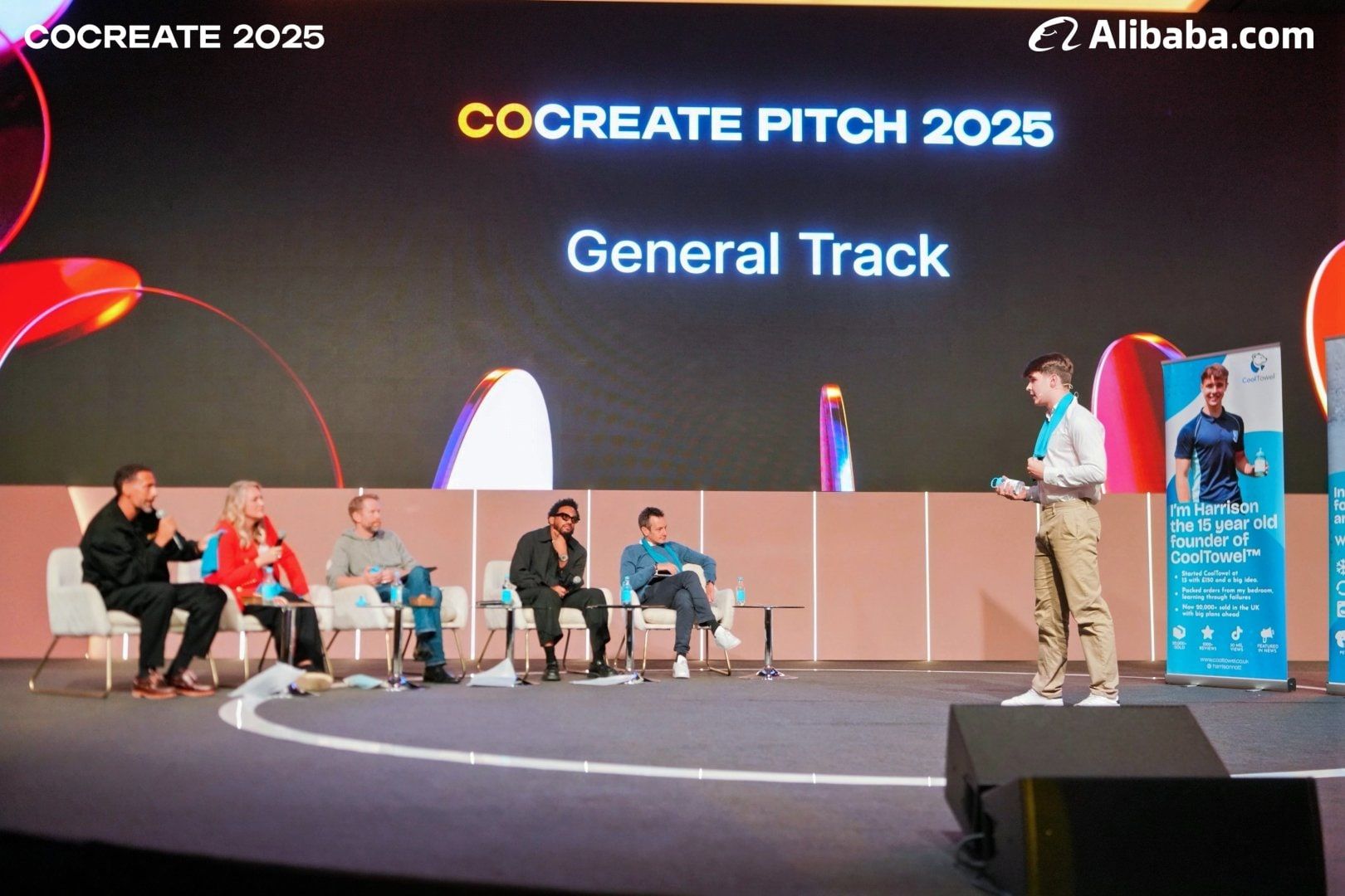 Harrison Nott standing on the CoCreate stage in front of the seated judging panel
