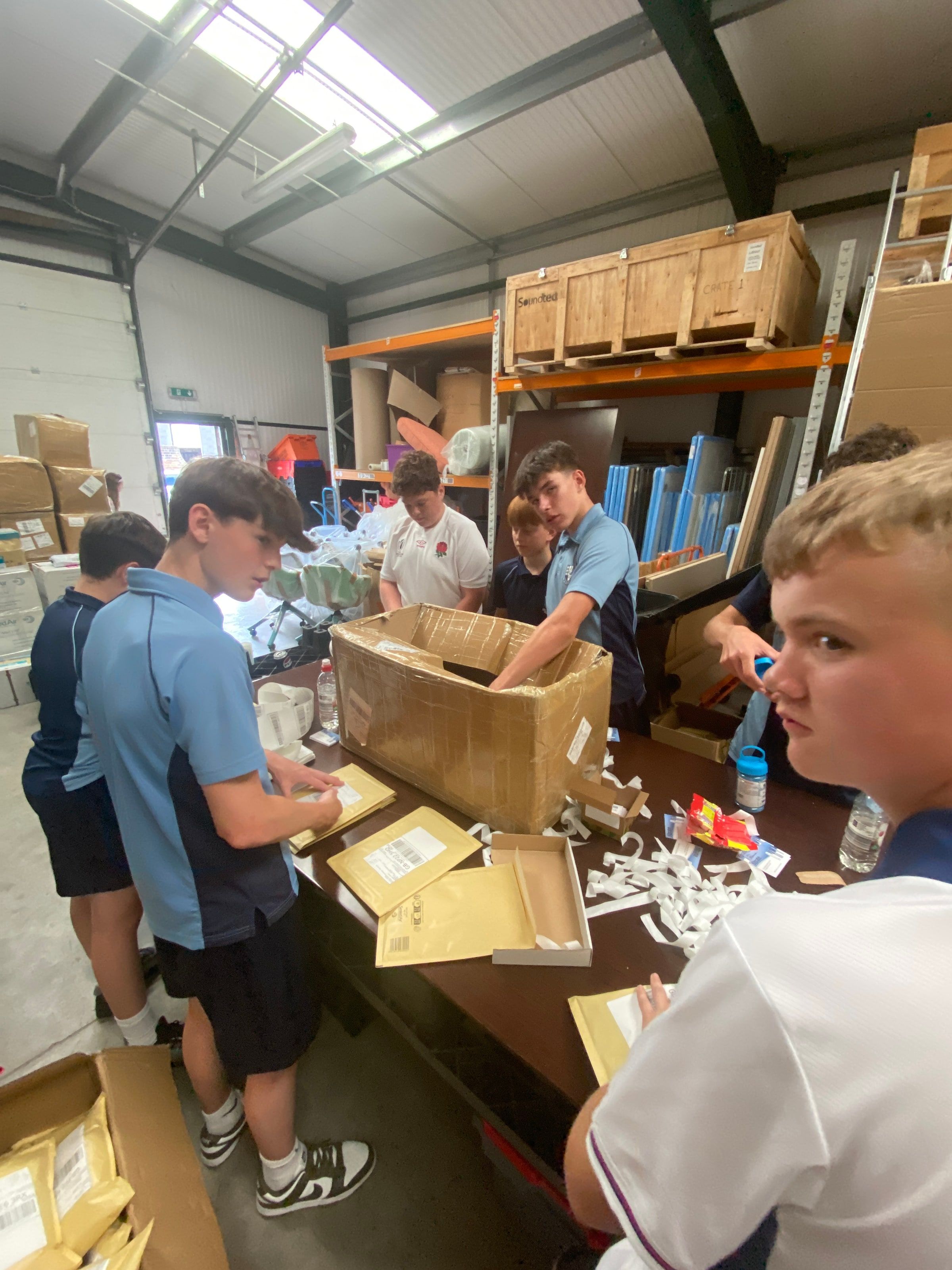 Seven of Harrison's school friends packing padded envelopes along a table in the warehouse unit