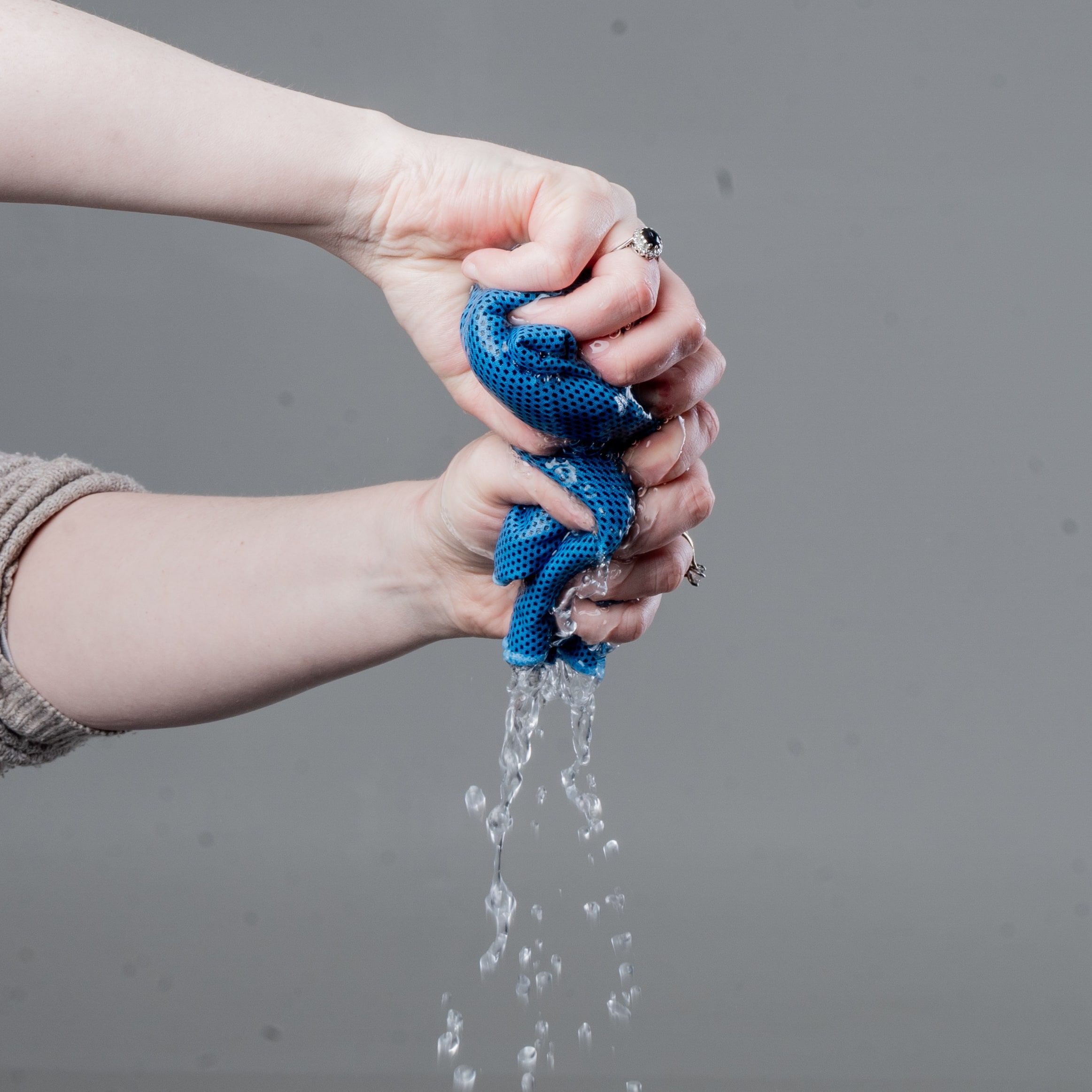 Two hands wringing water out of a blue CoolTowel