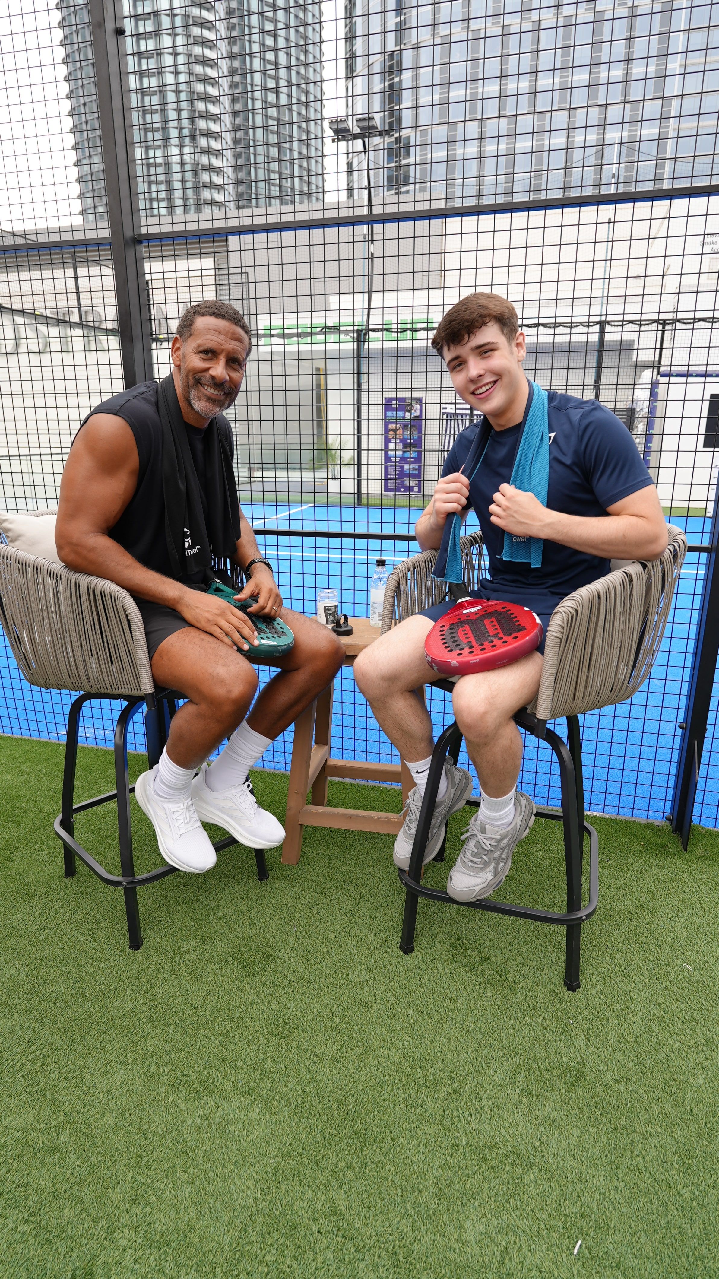 Harrison and Rio Ferdinand sitting courtside after padel, CoolTowels round their necks