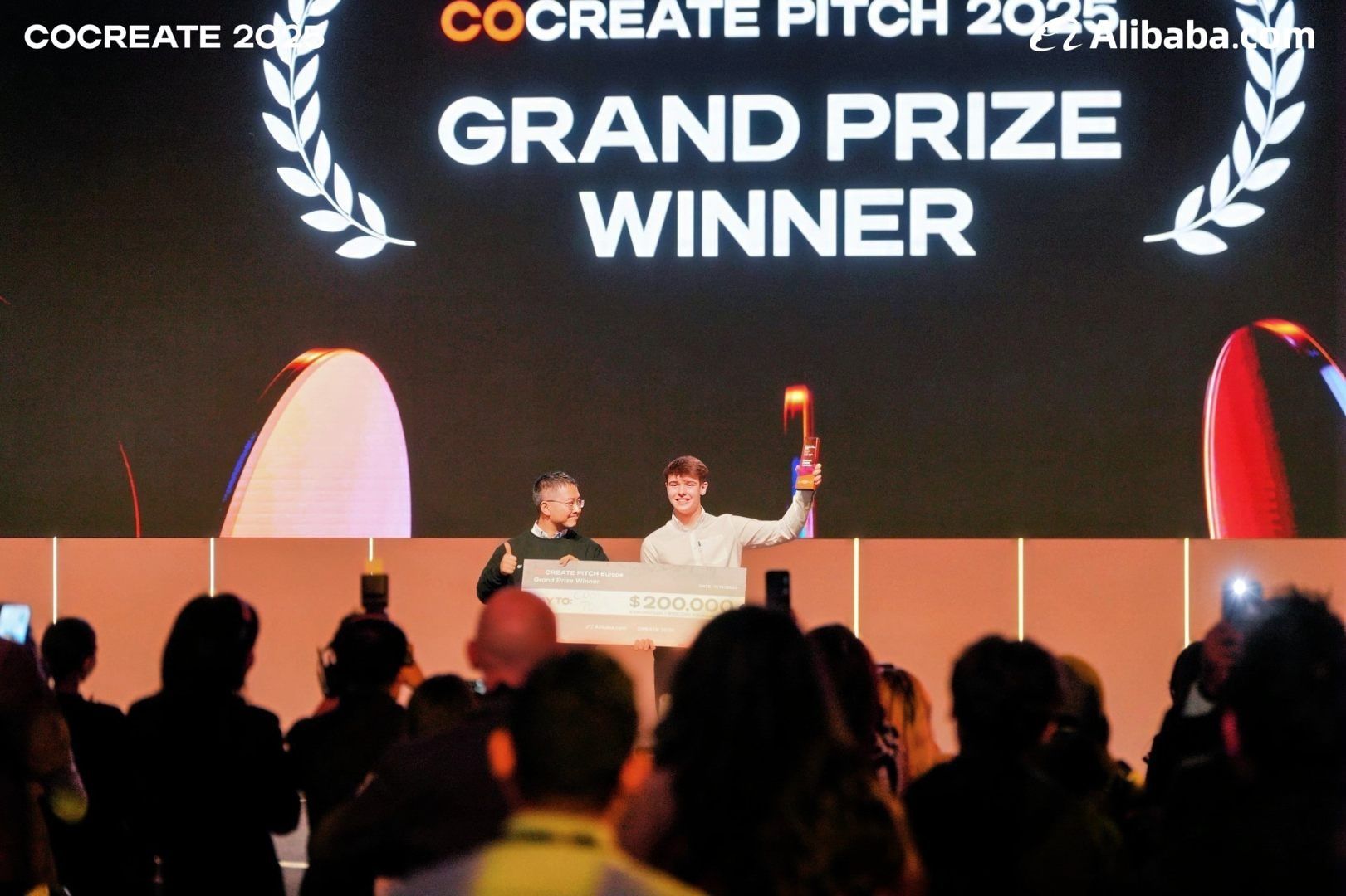 The stage screen reading Grand Prize Winner above Harrison and the cheque