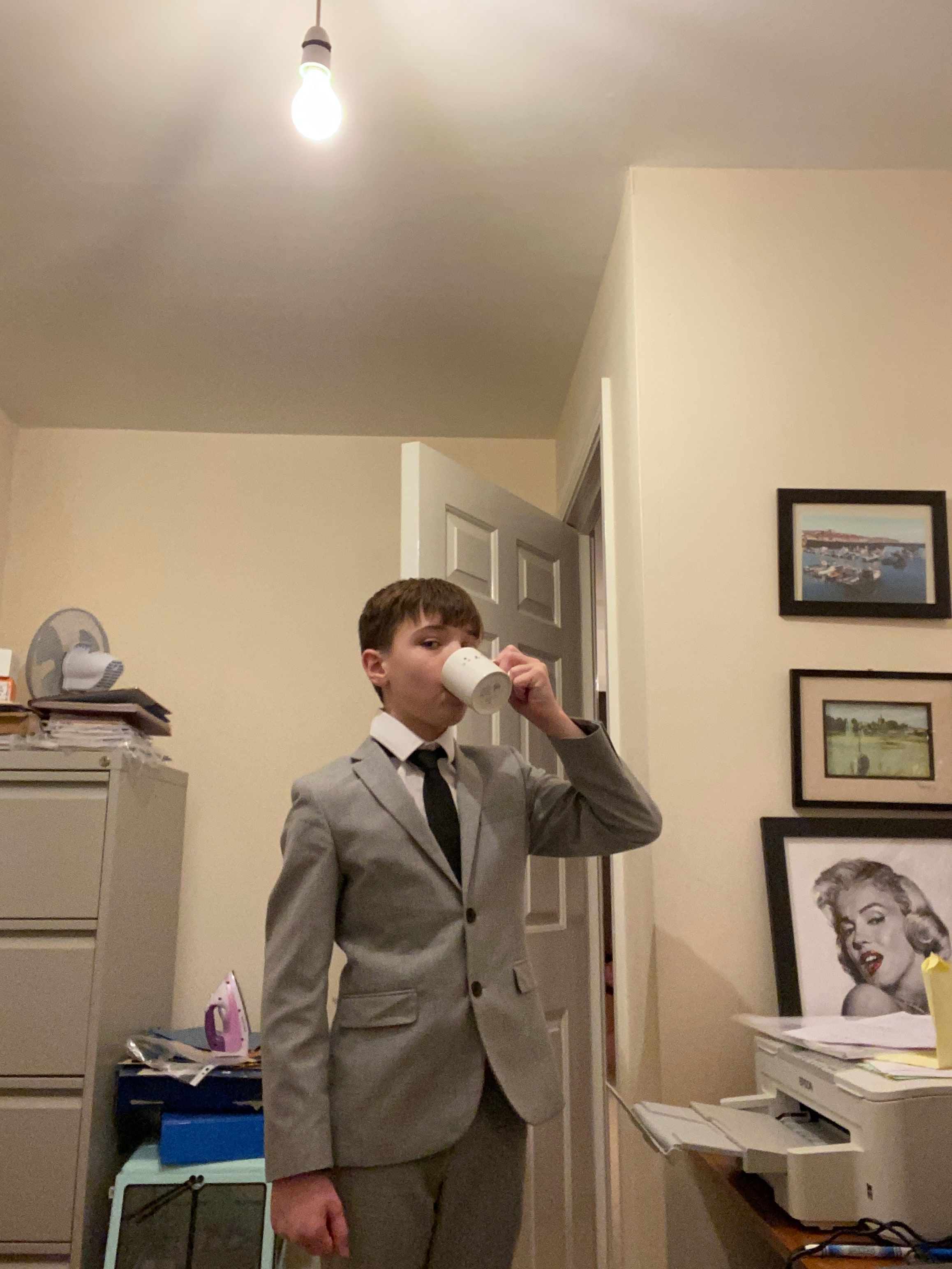 Harrison as a small boy in an oversized suit and tie, drinking from a mug